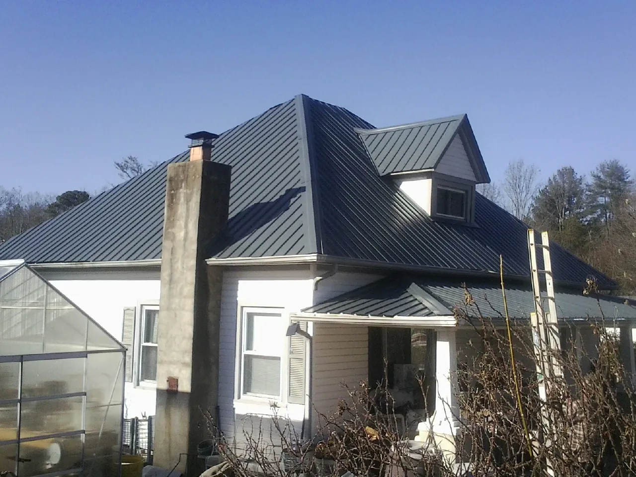 Dark blue standing seam metal roof on a white farmhouse with dormer — Slate & Tile Roof Repair by Roofing Brothers in Randall