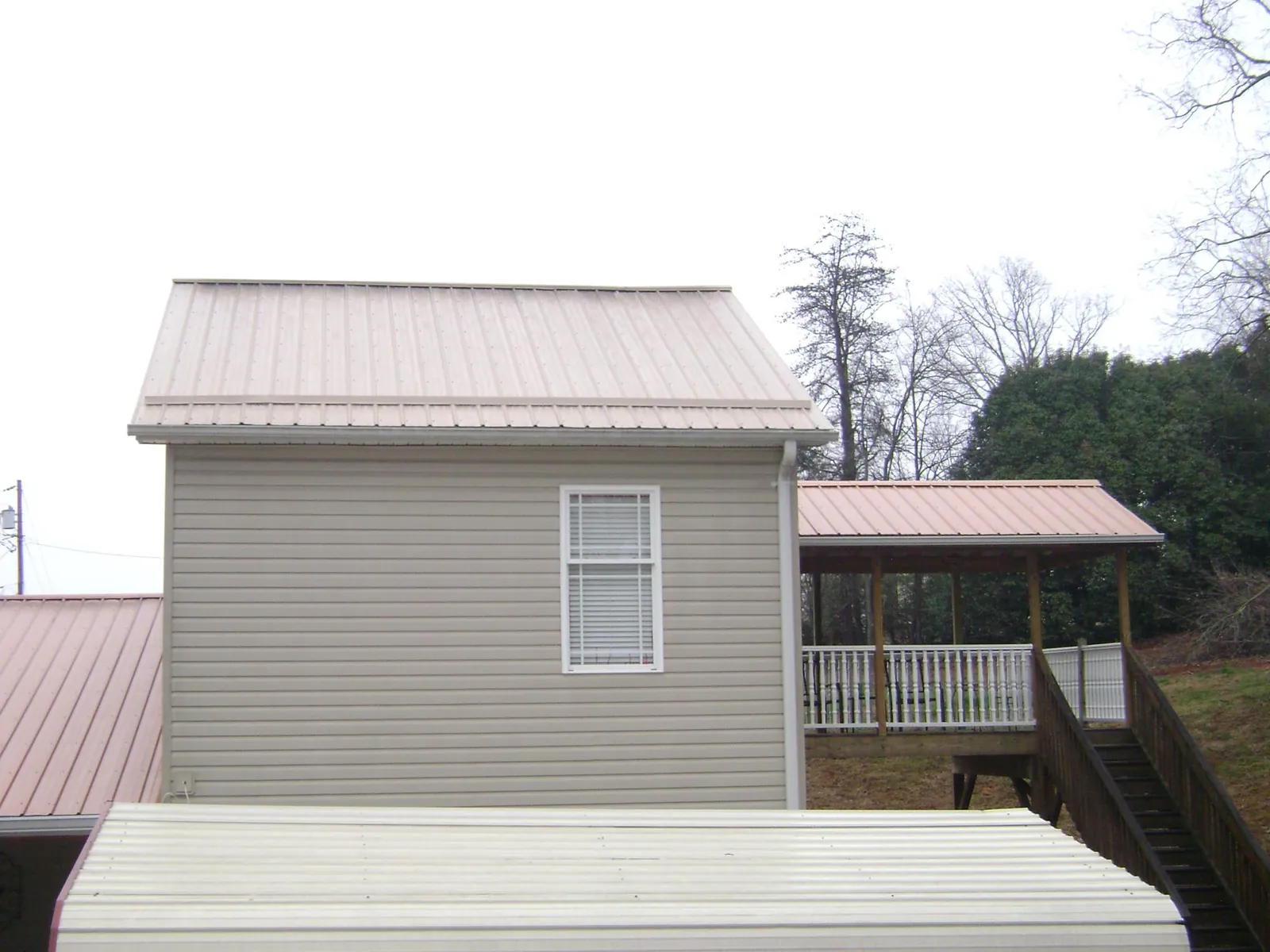 Tan metal roofs on a two story addition and attached porch, from a Roof Replacement job in Randall